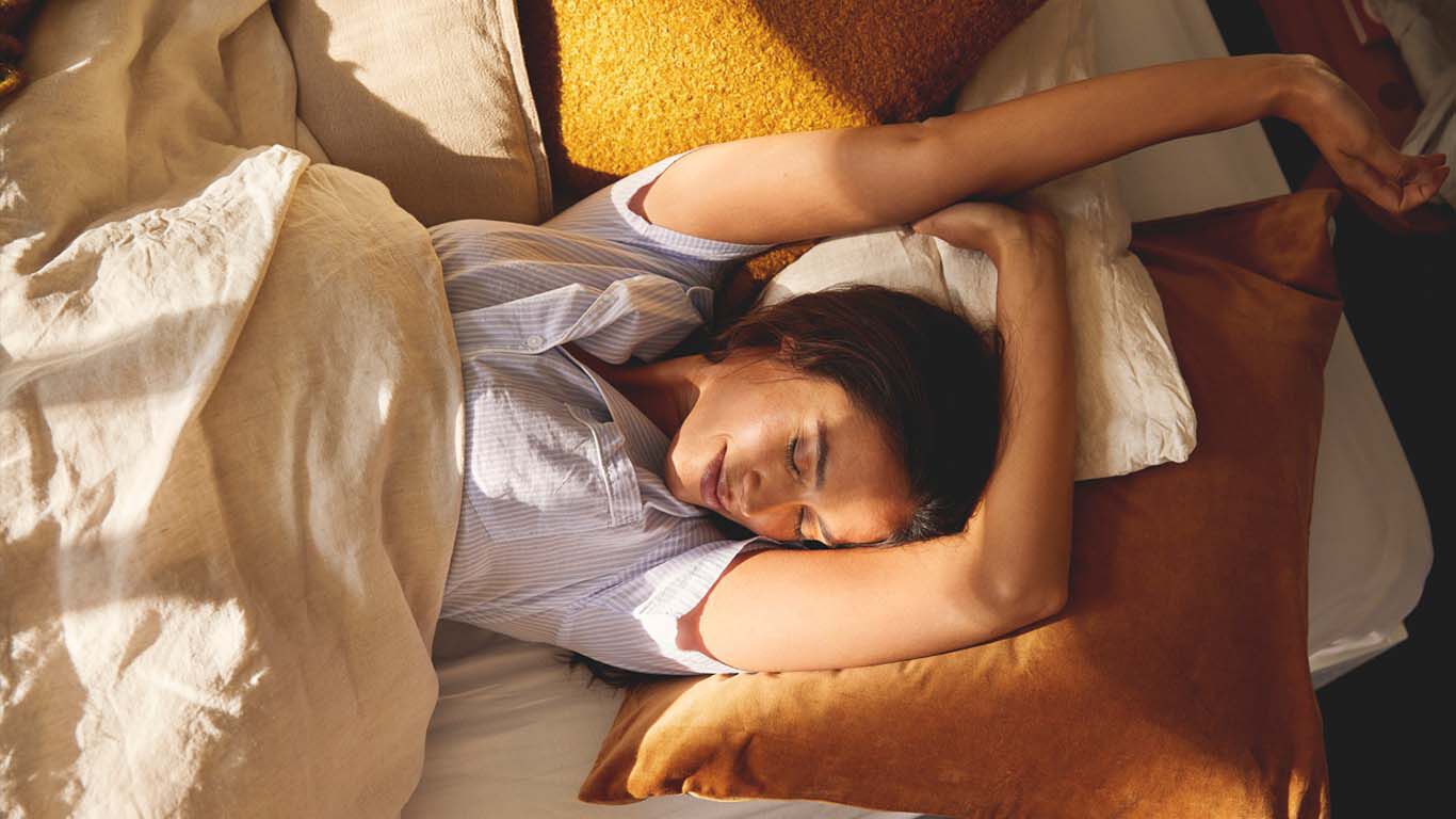 Une femme est allong&eacute;e, d&eacute;tendue, dans son lit et tend les bras jusqu'au bout du lit